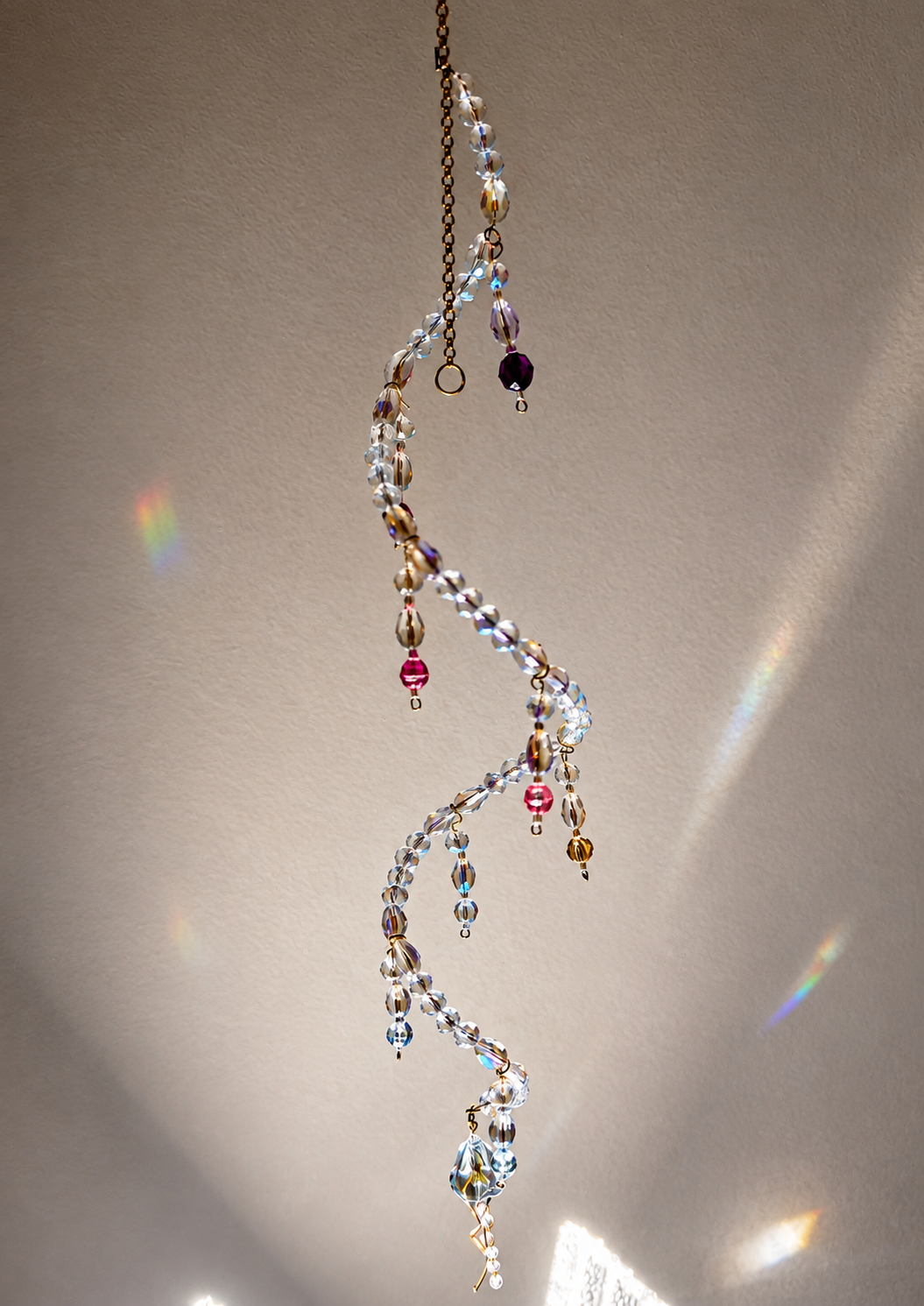 Hanging spiral suncatcher with clear faceted beads, purple and pink accents, and golden wire links